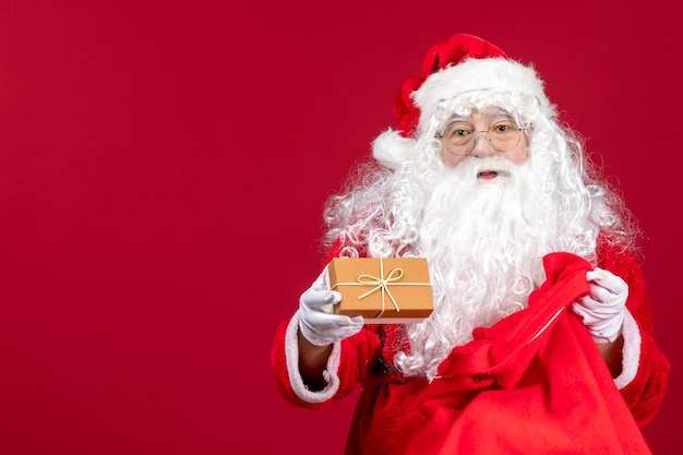 Vue de face du père noël tenant un cadeau d'un sac plein de cadeaux pour les enfants le noël du nouvel an rouge