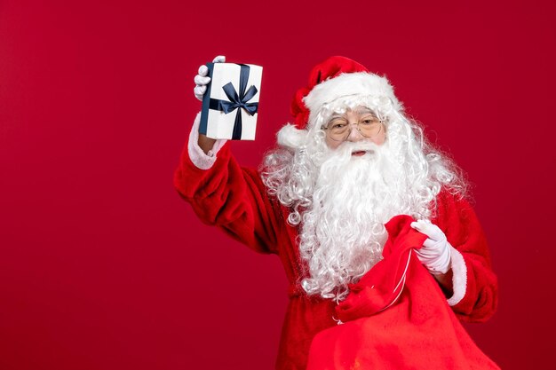 Vue de face du père noël tenant le cadeau d'un sac plein de cadeaux pour les enfants le noël du nouvel an rouge