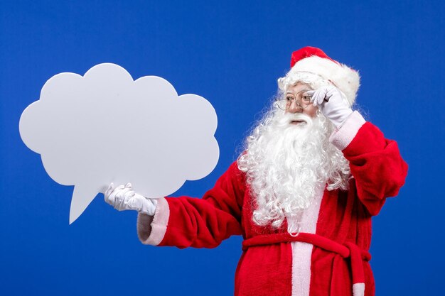 Vue de face du père noël tenant une grande pancarte en forme de nuage sur la couleur bleue des vacances de neige noël