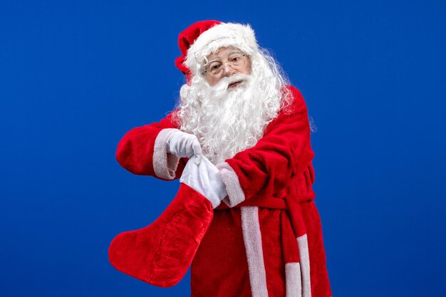 Vue de face du père noël tenant une grosse chaussette de noël sur la neige de noël de couleur de sol bleu