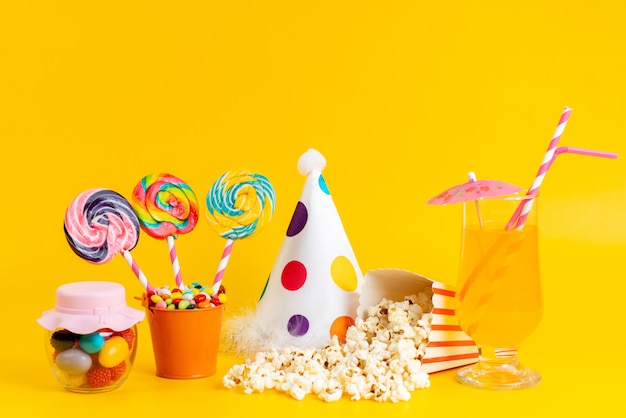 Une vue de face du pop-corn et des sucettes avec chapeau drôle et cocktail sur jaune