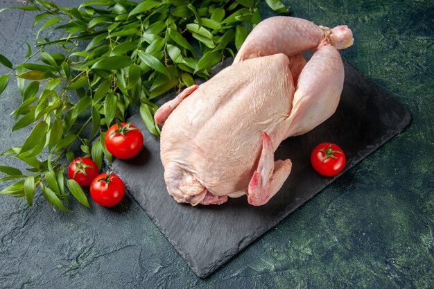 Vue de face du poulet cru frais avec des feuilles vertes sur un repas de poulet foncé viande animale photo cuisine couleur alimentaire