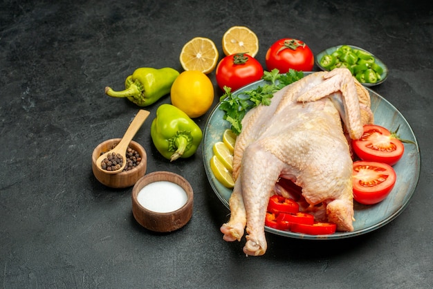 Vue de face du poulet cru frais à l'intérieur de la plaque avec du citron vert et des légumes sur fond sombre couleur de la nourriture photo de la viande animal oiseau