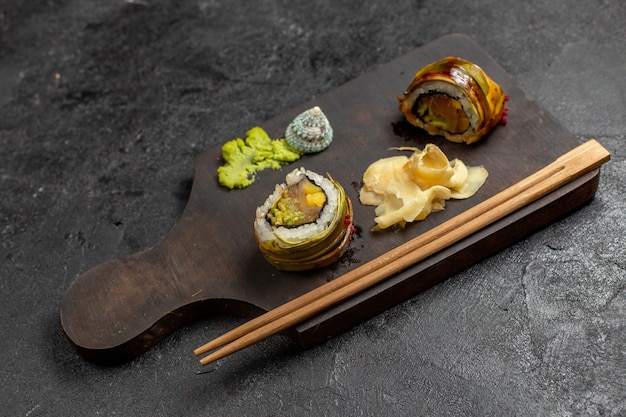 Vue de face du savoureux repas de sushi en tranches de poisson avec du wassabi vert et des bâtons sur mur gris