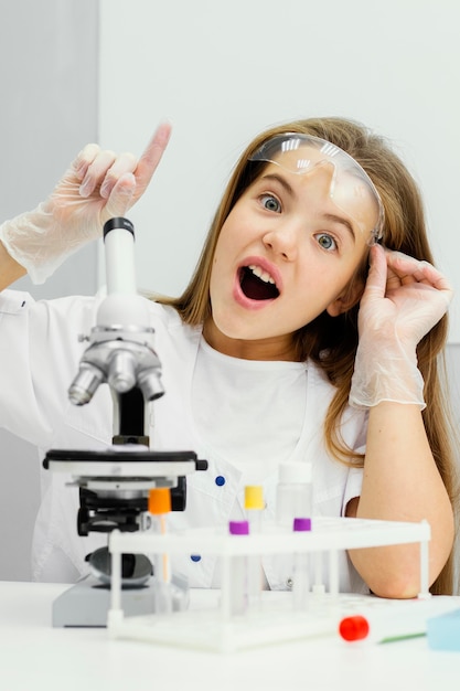 Vue de face du scientifique de la jeune fille à l'aide d'un microscope et ayant une idée