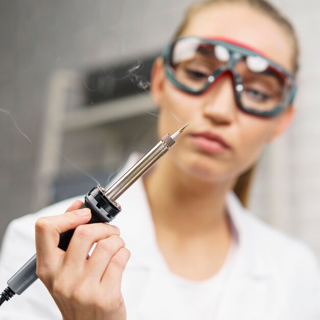 Vue de face du technicien féminin avec fer à souder et lunettes de sécurité