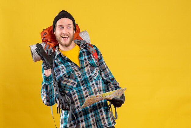 Vue de face du touriste masculin heureux avec des gants en cuir et sac à dos tenant la carte en agitant la main