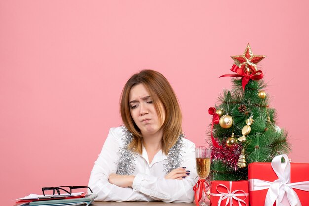 Vue de face du travailleur féminin assis autour de cadeaux de Noël sur rose