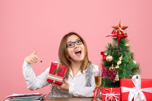 Vue de face du travailleur féminin assis avec des cadeaux de Noël sur rose