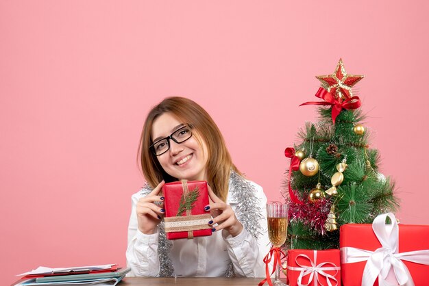 Vue de face du travailleur féminin assis avec des cadeaux de Noël sur rose
