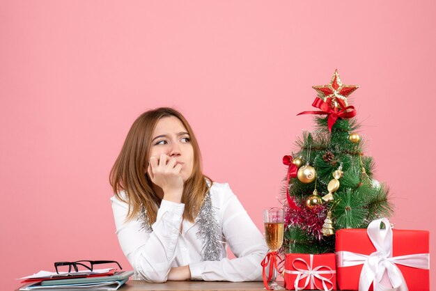 Vue de face du travailleur féminin assis avec des cadeaux sur la table rose