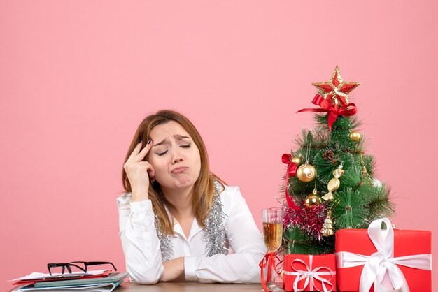 Vue de face du travailleur féminin assis avec des cadeaux sur la table rose