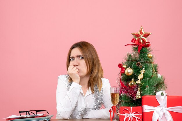 Vue de face du travailleur féminin assis derrière sa table avec des cadeaux sur rose