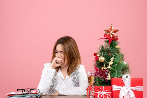 Vue de face du travailleur féminin assis derrière sa table avec des cadeaux sur rose