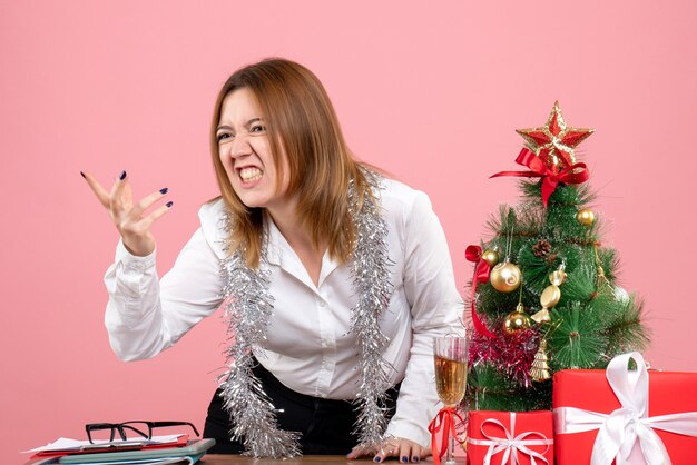 Vue de face du travailleur féminin autour de cadeaux de Noël faisant valoir sur rose