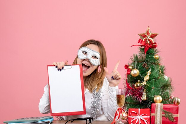 Vue de face du travailleur féminin en masque de fête avec note de fichier sur rose