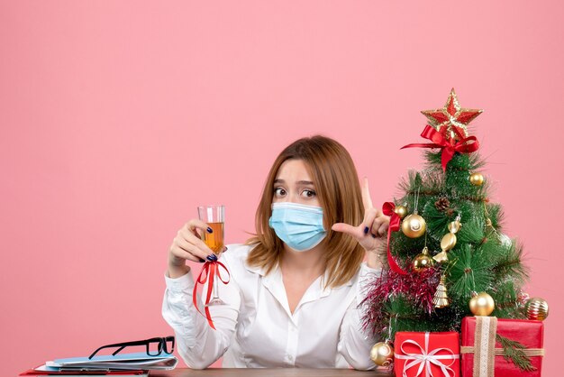 Vue de face du travailleur féminin en masque stérile célébrant Noël avec champagne sur rose