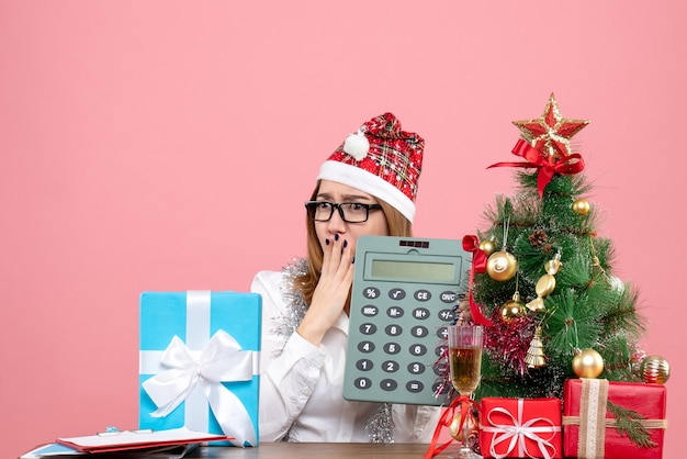 Vue de face du travailleur féminin tenant la calculatrice autour de cadeaux sur rose