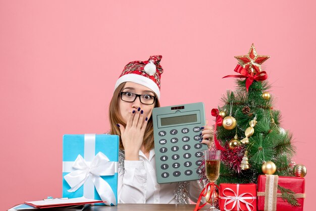 Vue de face du travailleur féminin tenant la calculatrice autour de cadeaux sur rose