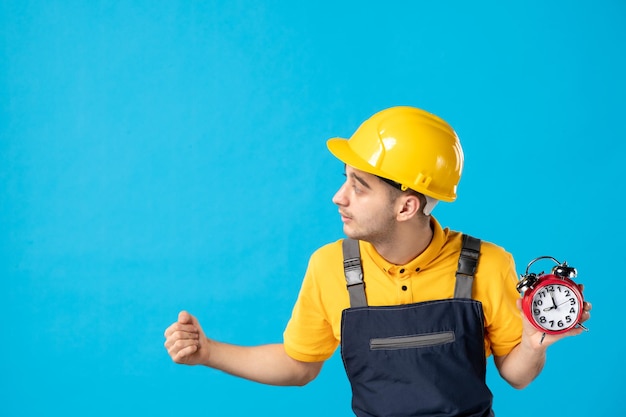 Vue de face du travailleur masculin en uniforme jaune avec des horloges sur bleu