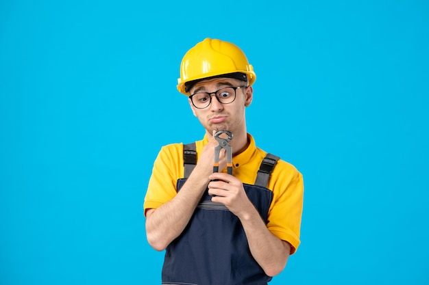 Vue de face du travailleur masculin en uniforme jaune avec des pinces dans ses mains sur bleu