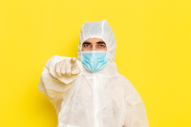 Vue de face du travailleur scientifique masculin en combinaison blanche de protection spéciale avec masque sur le mur jaune clair