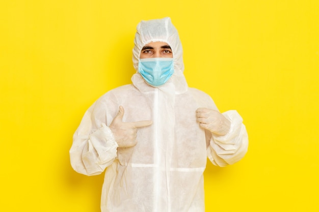 Vue de face du travailleur scientifique masculin en tenue de protection spéciale et avec masque sur le mur jaune clair
