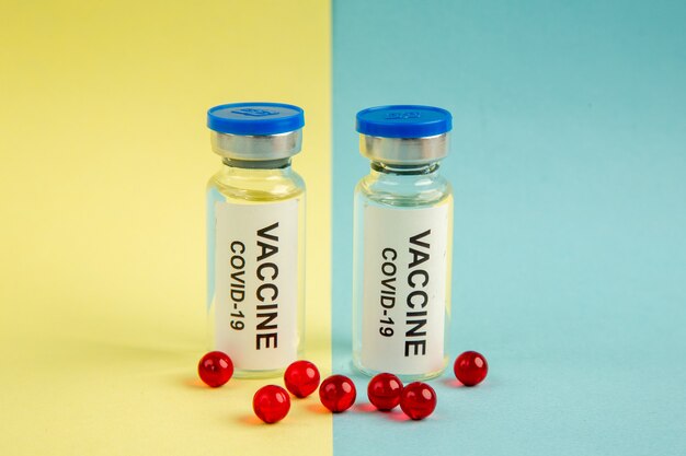 Vue de face du vaccin contre le coronavirus avec des pilules rouges sur fond jaune-bleu virus pandémie couleurs laboratoire de santé covid- médicament scientifique hospitalier
