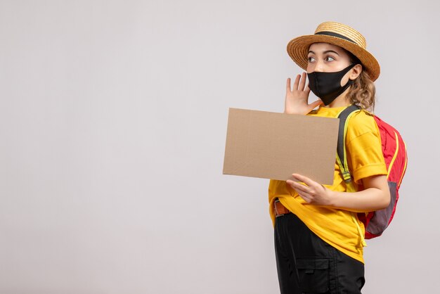 Vue de face du voyageur féminin avec sac à dos tenant carton sur mur gris