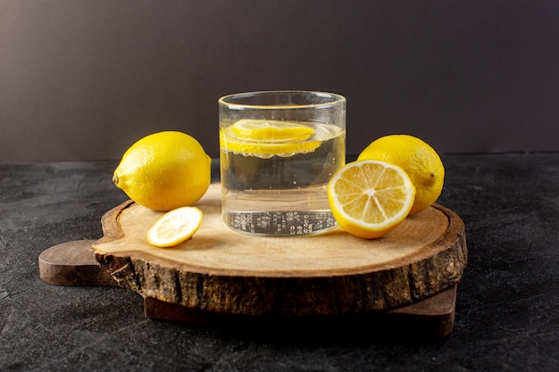 Une vue de face de l'eau avec du citron boisson fraîche fraîche avec des citrons tranchés avec des citrons entiers à l'intérieur de verres transparents sur l'obscurité