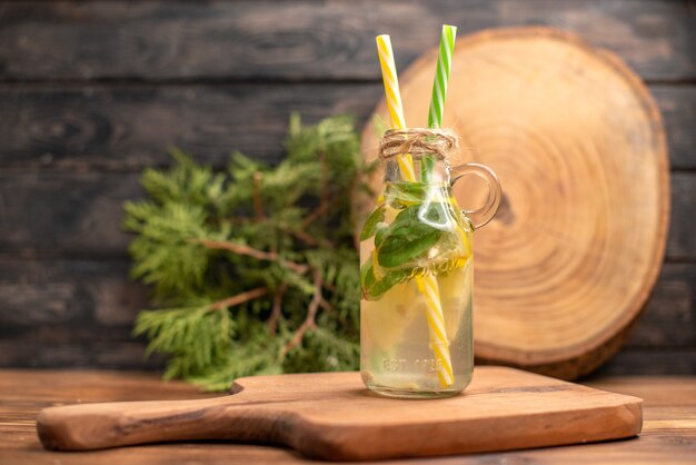 Vue de face de l'eau fraîche de désintoxication dans un verre servi avec des tubes sur une planche à découper en bois sur une table marron