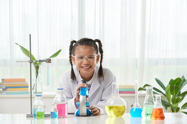 Vue de face d'une écolière en robe de laboratoire faisant l'expérience chimique