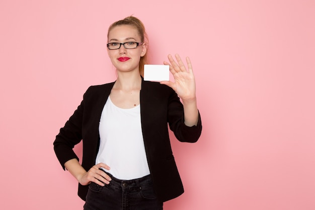 Vue de face de l'employé de bureau en veste noire stricte souriant tenant une carte blanche sur un mur rose