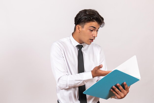 Vue de face employé masculin vérifiant les documents sur le travail de travail d'affaires masculin de mur blanc