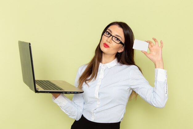 Vue de face de l'employée de bureau en chemise blanche et jupe noire à l'aide de son ordinateur portable sur le mur vert clair