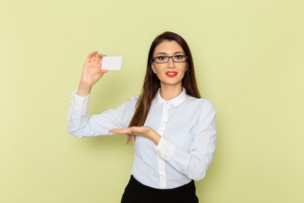 Vue de face de l'employée de bureau en chemise blanche et jupe noire tenant une carte en plastique blanc sur un mur vert clair
