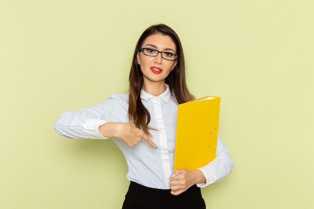 Vue de face de l'employée de bureau en chemise blanche et jupe noire tenant un fichier jaune sur le mur vert