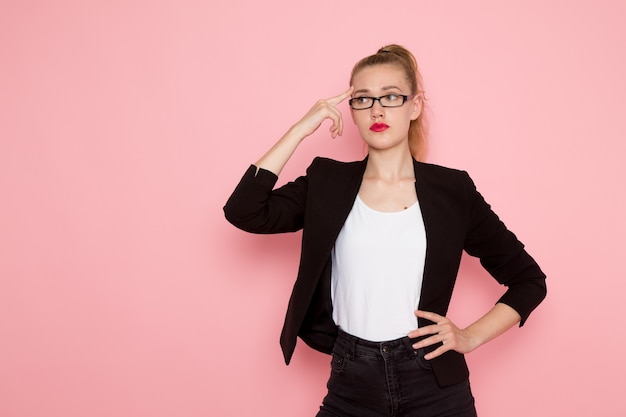 Vue de face de l'employée de bureau en veste noire stricte pensée sur le mur rose clair