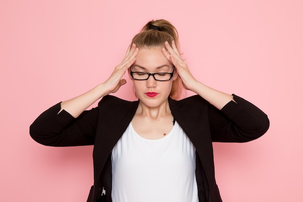 Vue de face de l'employée de bureau en veste noire stricte posant avec une expression fatiguée sur un mur rose clair