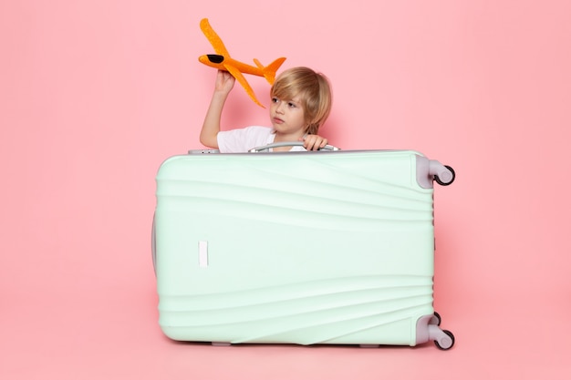 Vue de face enfant blond tenant un avion orange sur le bureau rose