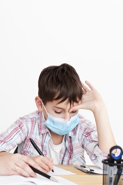 Vue de face de l'enfant faisant ses devoirs tout en portant un masque médical