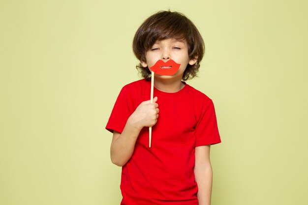 Une vue de face enfant garçon en t-shirt rouge tenant les lèvres collent sur l'espace de couleur pierre