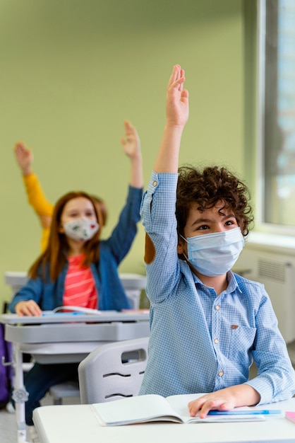 Vue de face des enfants levant la main en classe