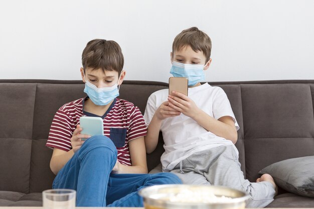 Vue de face des enfants avec des masques médicaux jouant sur les smartphones