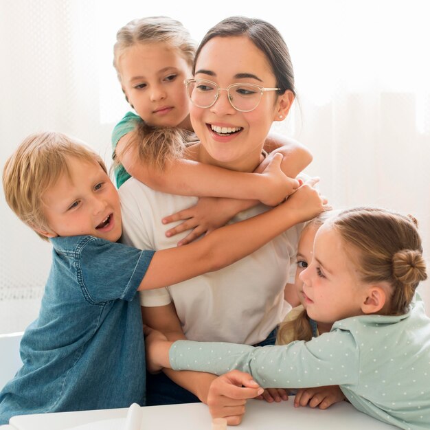 Vue de face des enfants serrant leur professeur