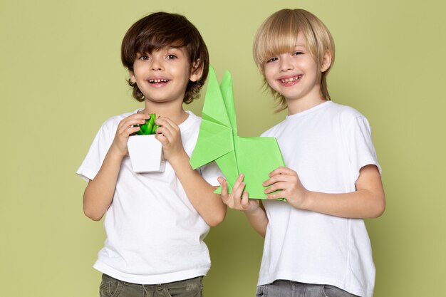 Une vue de face des enfants souriants en t-shirts blancs tenant des chiffres en papier et une petite plante verte sur l'espace de couleur pierre