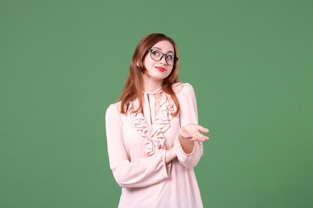 Vue de face enseignante en chemisier rose sur fond vert bibliothèque collège leçon couleurs travail livre emploi jeune femme élève de l'école