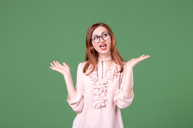 Vue de face enseignante en chemisier rose sur fond vert bibliothèque de l'école collège leçon couleurs livre de travail femme étudiant emploi jeune