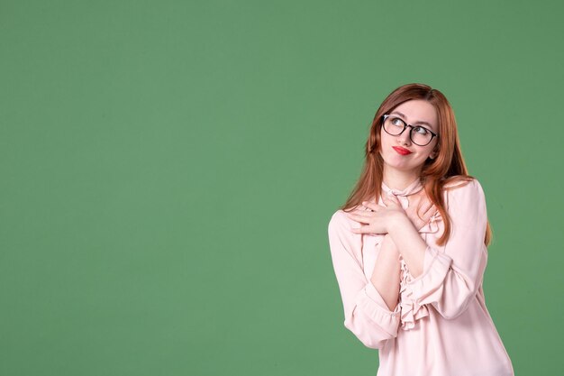 Vue de face enseignante en chemisier rose posant sur fond vert emploi école femme couleur livre jeunes étudiants bibliothèque collège leçon de travail