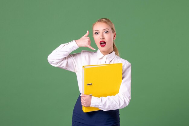 Vue de face enseignante posant dans des vêtements stricts avec des fichiers jaunes sur fond vert travail étudiant livre école université femme bibliothèque leçon de couleurs